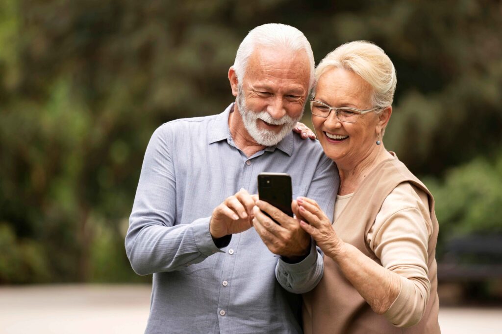Dos personas mayores sonriendo mirando su móvil