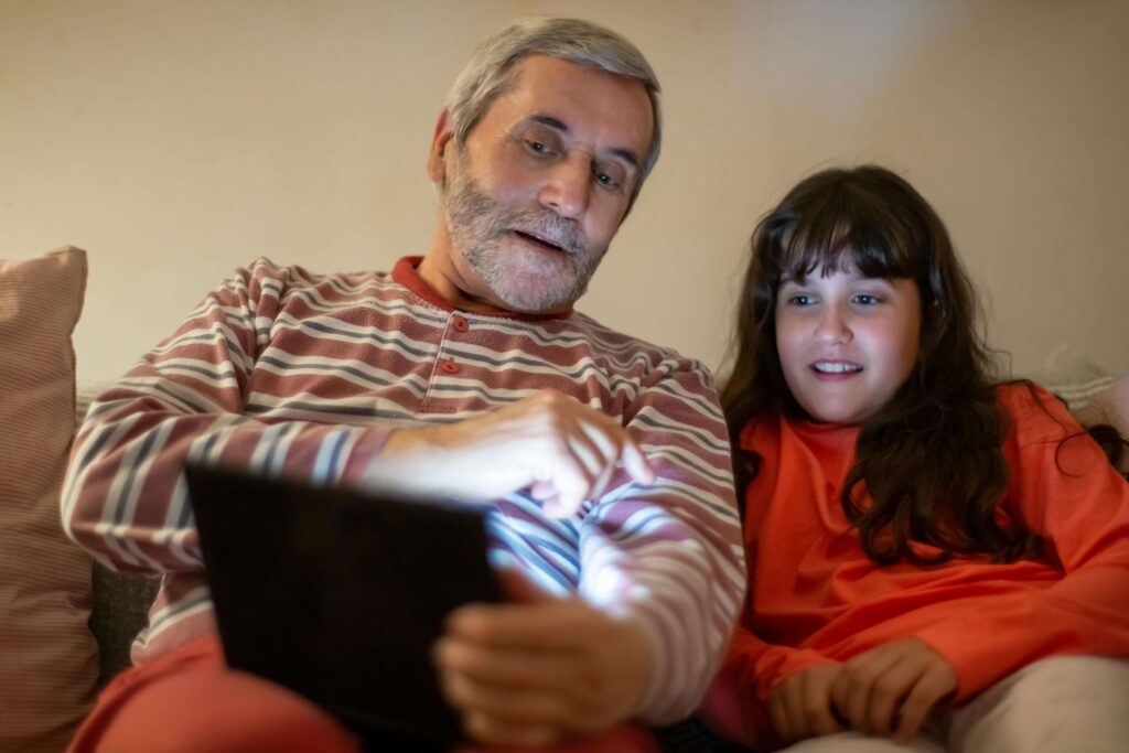 Un hombre mayor usando una tablet con su nieta